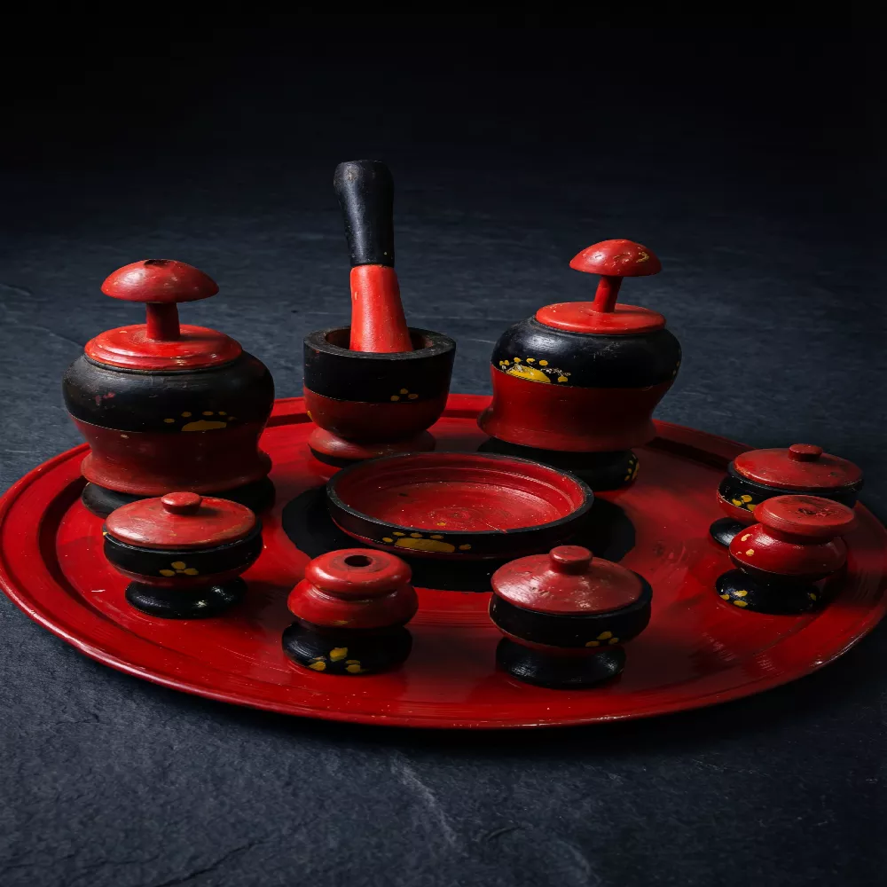 صينية جرتق سودانية تقليدية من الخشب المنقوش باللونين الأحمر والأسود، تضم مبخر وعلب بخور وعطور تراثية بتصميم يدوي فخم على خلفية داكنة.